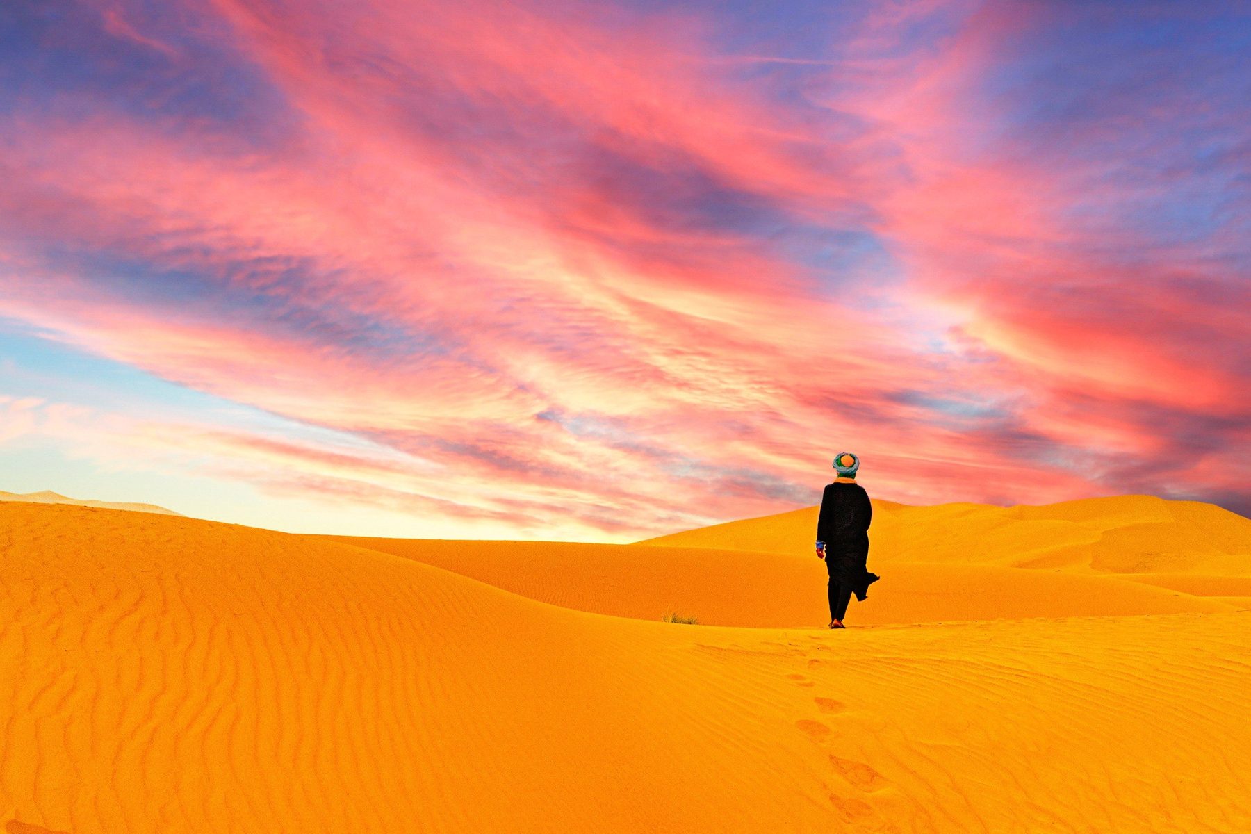 Una persona attraversa le dune del Sahara al tramonto